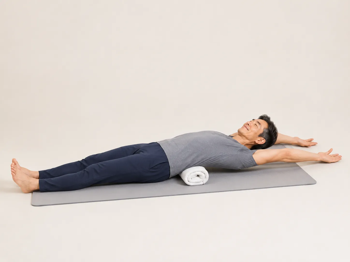 Older adult lying on a mat with a rolled towel under the lower back and arms stretched overhead, easing lumbar tension